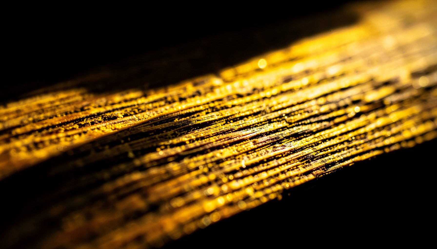 Extreme close-up photograph of weathered wood grain on a sunlit timber beam, with deep amber highlights and shadowed grooves